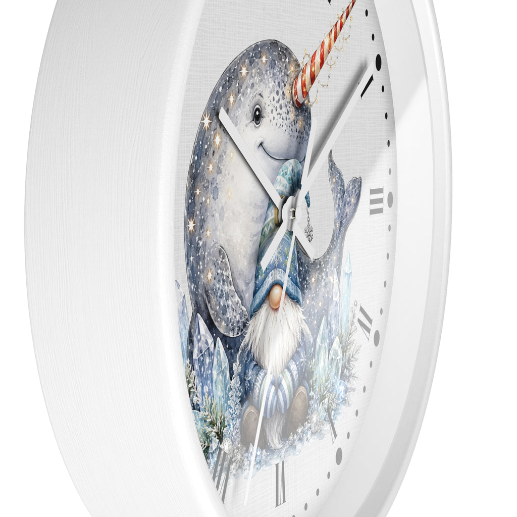 A white round wall clock featuring a whimsical illustration of a gray narwhal with a striped red-and-white horn and a blue-clad gnome with a white beard, set against a snowy icy background with gold stars.