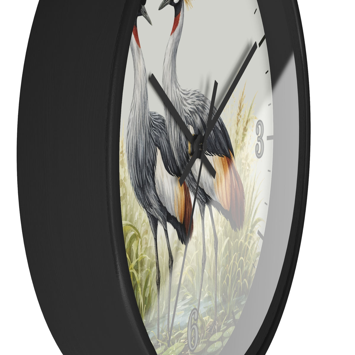 A close-up of a round wall clock with a black frame and a printed dial showing two gray cranes standing in a grassy scene. The clock is photographed against a plain white background.