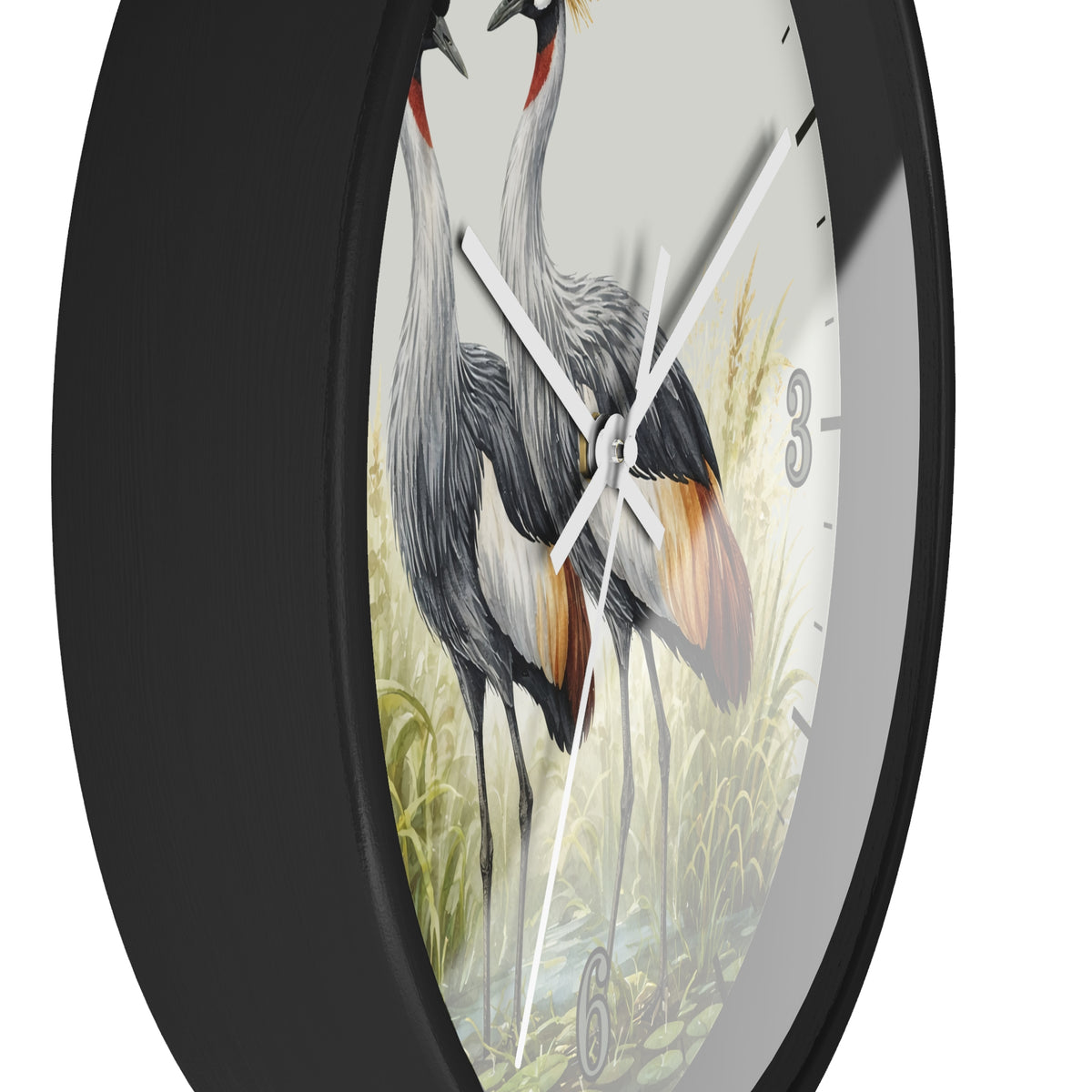 A close-up of a round wall clock with a black frame and a printed bird illustration on the face. The artwork shows two gray cranes with orange and yellow accents among green reeds on a light background.