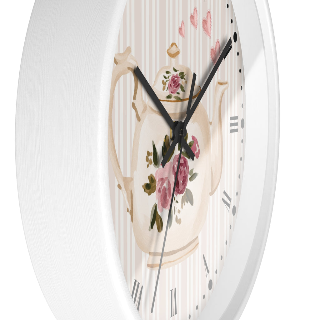 A close-up of a round wall clock with a white frame and a decorative dial featuring a cream teapot with pink roses, green leaves, and a striped background.