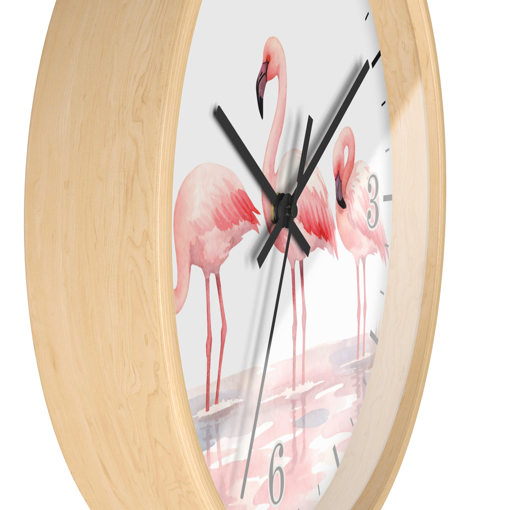 Round wall clock with a light natural wood frame and a white dial printed with pink flamingos standing in shallow water. Black clock hands and partial black numerals are visible against a plain white background.