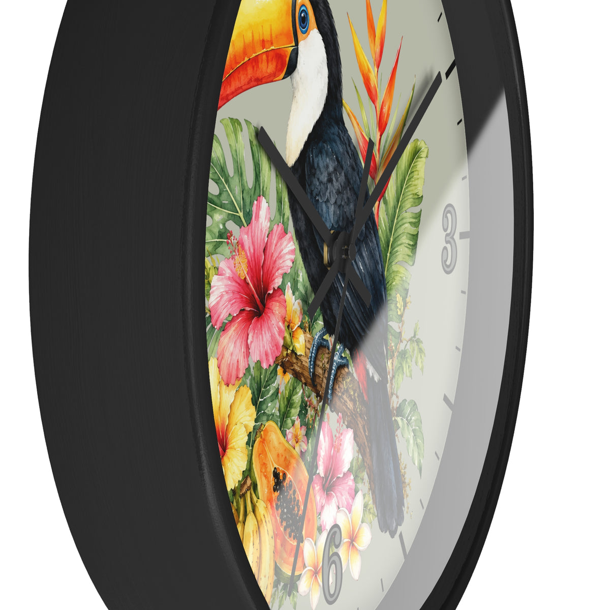 A close-up of a round wall clock with a black frame and a tropical print featuring a toucan, hibiscus flowers, and green leaves on a white dial.