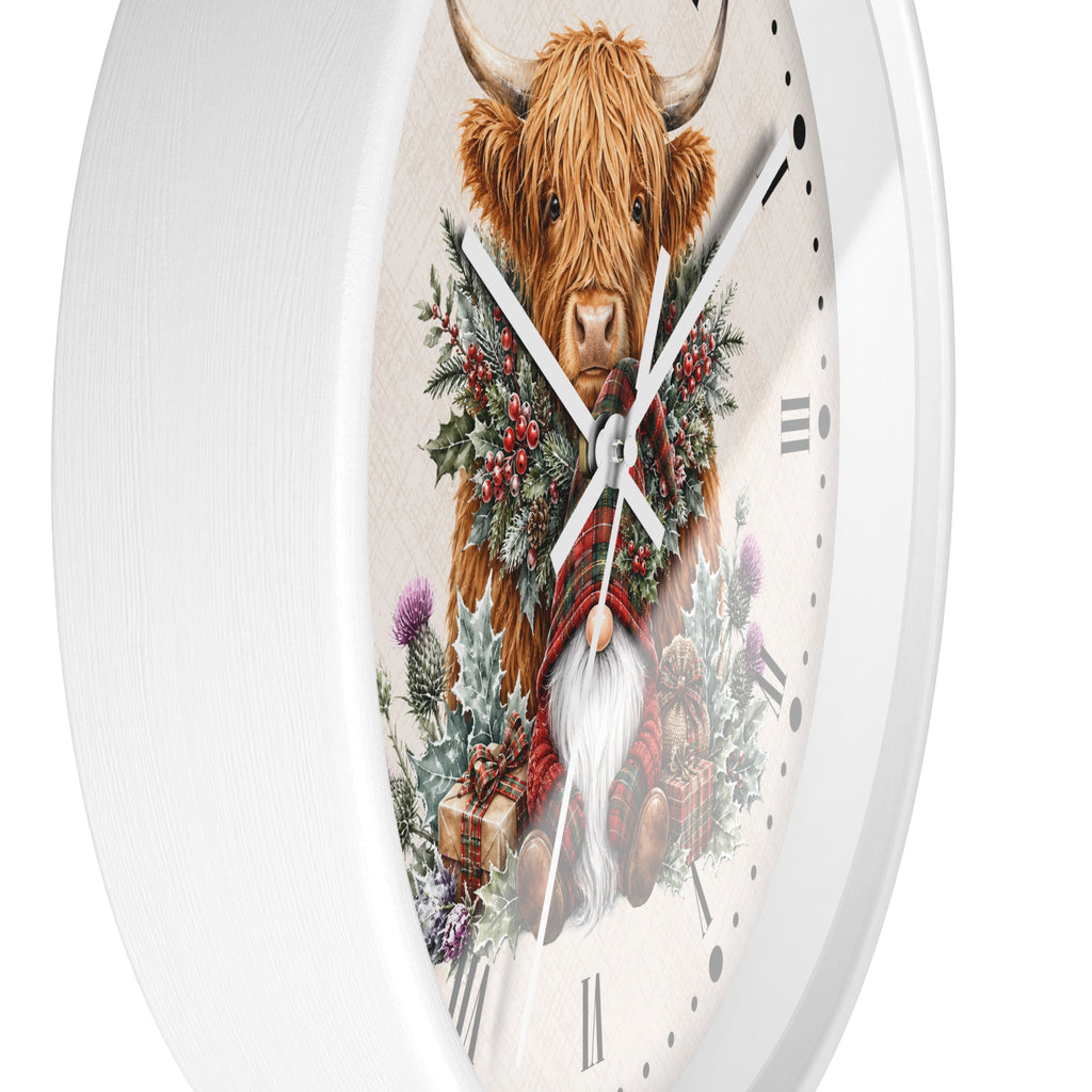 A white round wall clock featuring a detailed illustration of a Highland cow surrounded by a green and red winter wreath, set against a clean white background.
