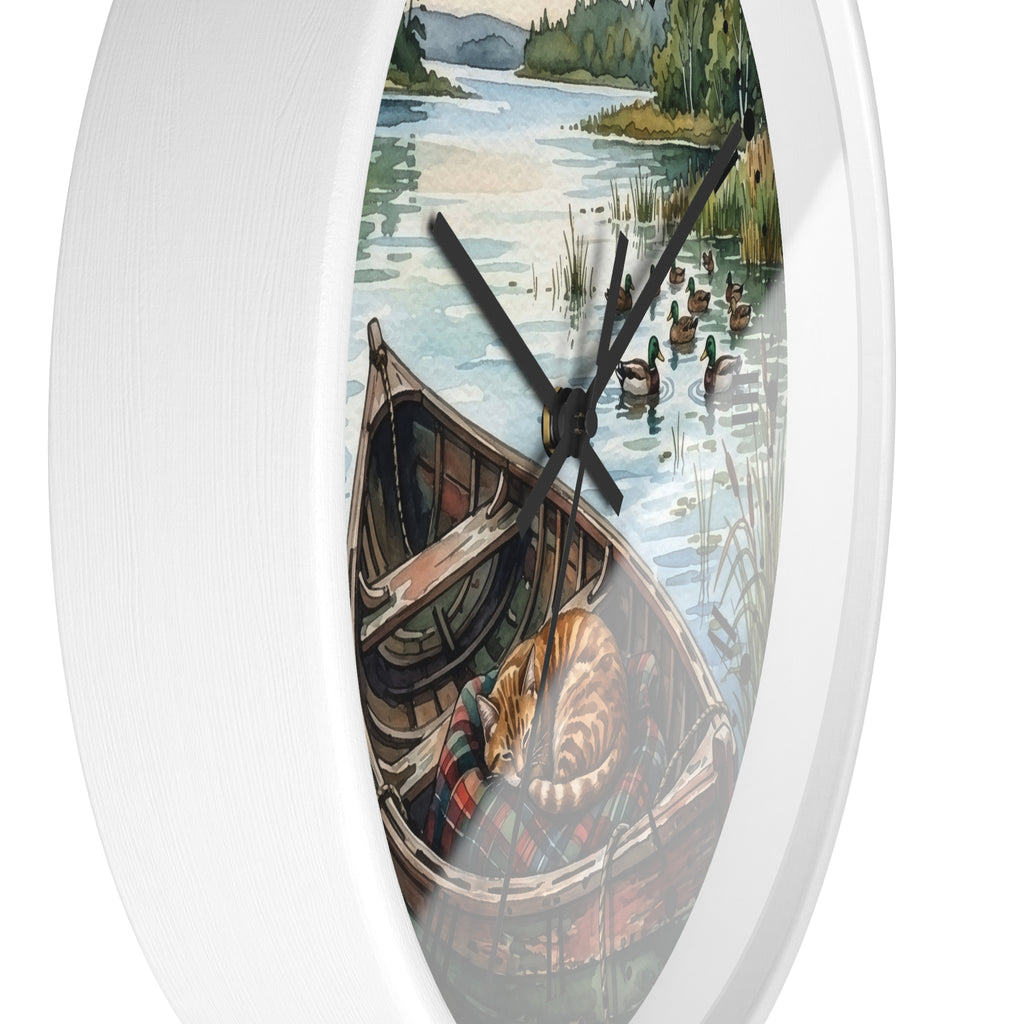 Oval white wall clock featuring a scenic illustration of a lake with ducks, a rowboat, and a sleeping cat, with black clock hands.