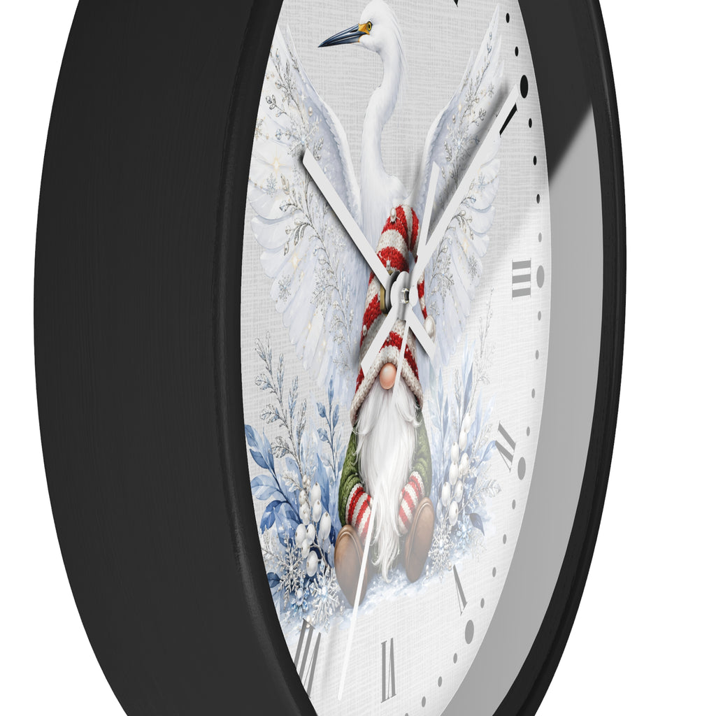 A close-up of a wall clock with a black frame and a white dial featuring a whimsical winter illustration: a white bird at the top, a small gnome wrapped in a red-and-white striped scarf and green pants near the bottom, and blue floral motifs around the dial.