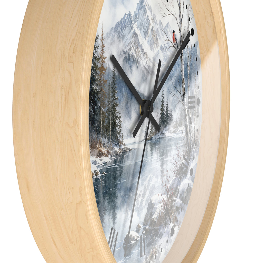 Round wall clock with a light natural wood frame and a printed winter landscape face showing snow-covered mountains, trees, and a frozen river, with black hands and no numerals.