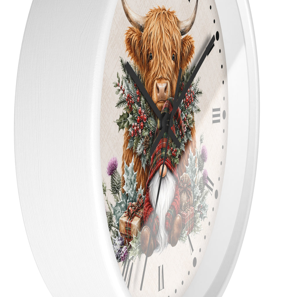 A white round wall clock featuring a festive illustration of a Highland cow with a red tartan plaid scarf, a white beard, and a green holly wreath with red berries on the clock face.