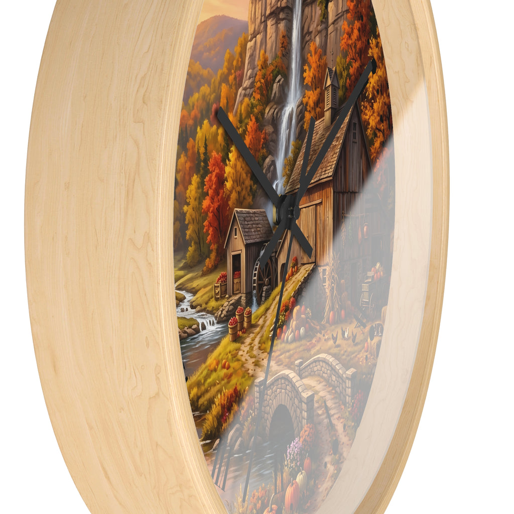 Round wall clock with a light natural wood frame and a scenic autumn landscape print featuring a waterfall, cabin, bridge, and colorful trees.