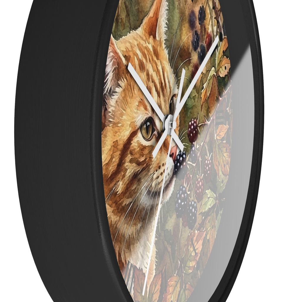 A round wall clock with a black frame and a printed design of an orange tabby cat over autumn leaves and blackberries on the face, shown against a plain white background.