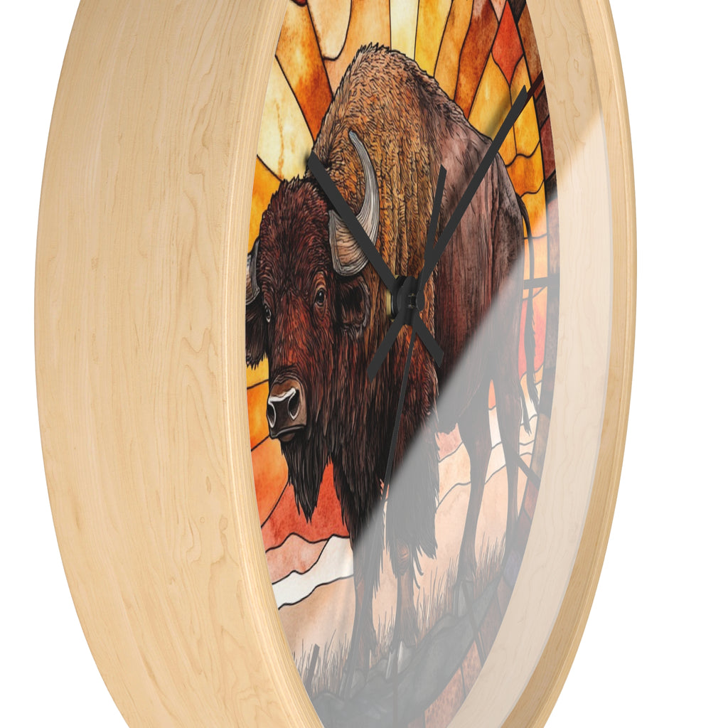 A round wall clock with a light natural wood frame and a stained-glass-style illustration of a bison in warm orange, yellow, brown, and red tones. The clock is shown at an angle against a plain white background.