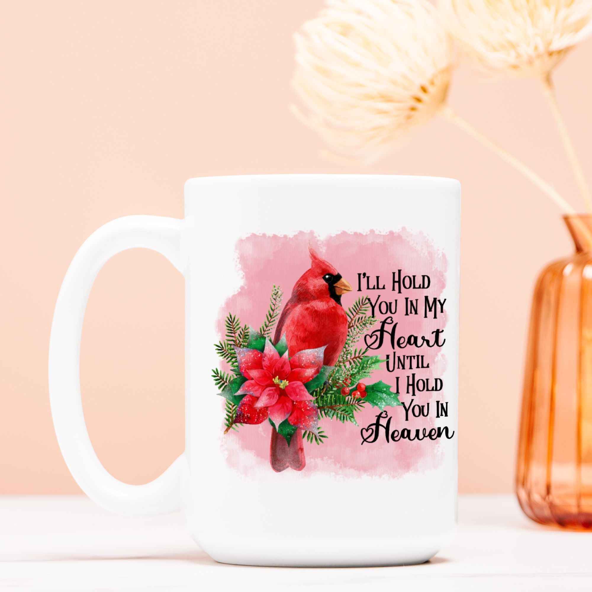 White mug with a red cardinal and floral design on a pink background, with text 'I'll Hold You In My Heart Until I Hold You In Heaven'.