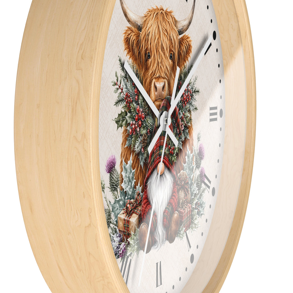 A round wall clock with a light natural wood frame and a whimsical illustration of a shaggy Highland cow wearing a red plaid scarf and green holly wreath, set against a clean white background.