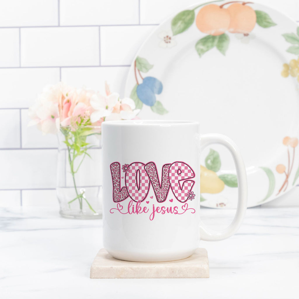 White mug with 'Love like Jesus' text on a white surface with a floral plate in the background.