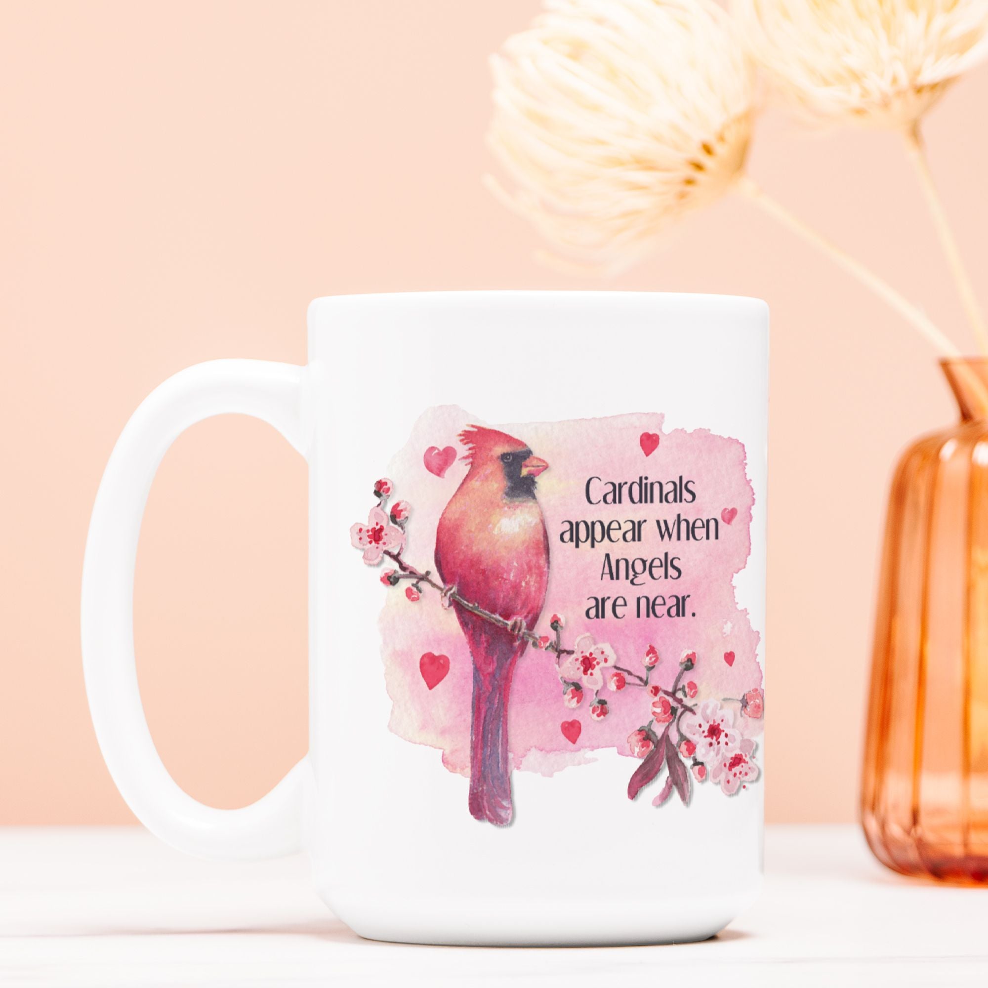 White mug with a pink cardinal design and text on a peach background