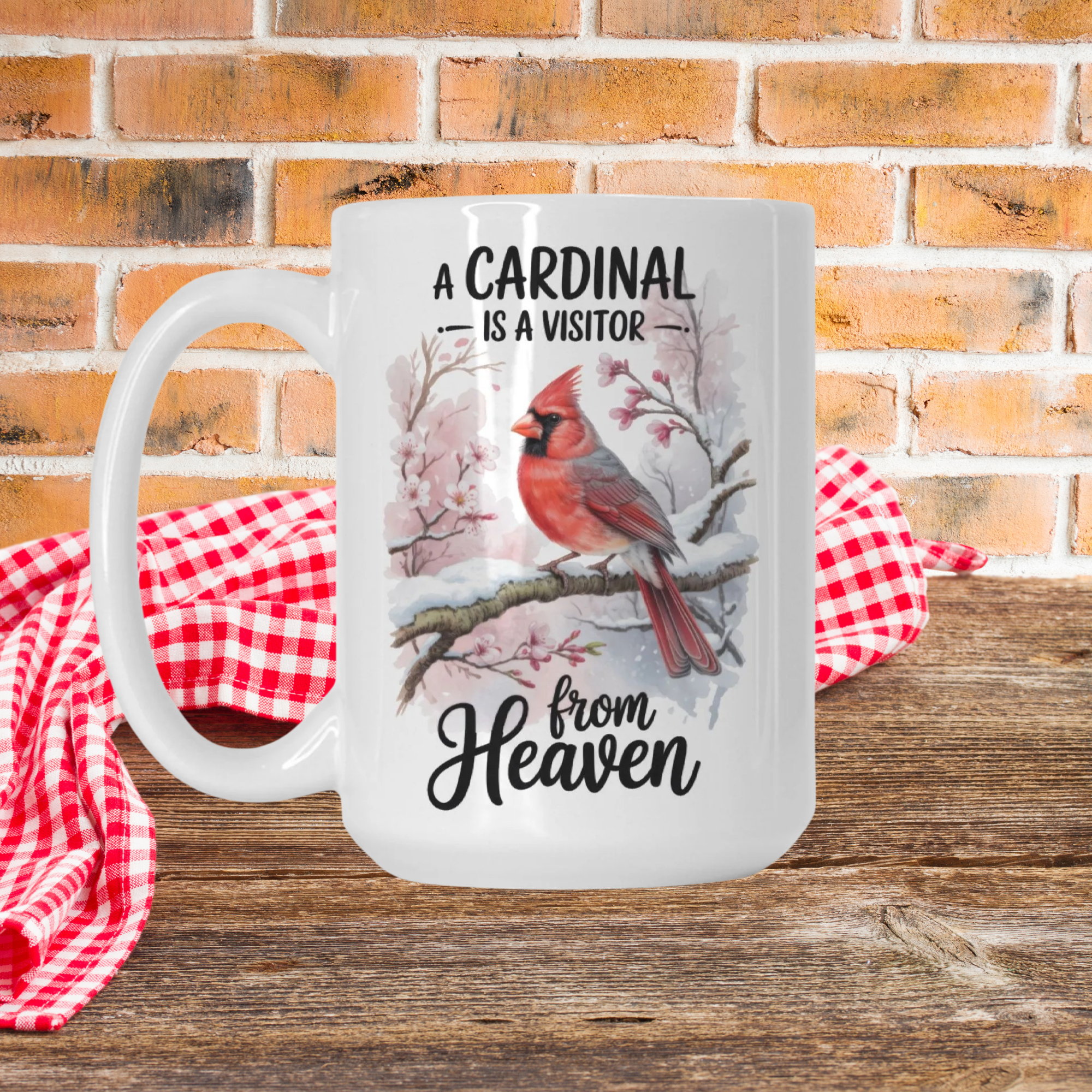 White mug with cardinal design and text on a wooden surface with a red checkered cloth and brick wall background