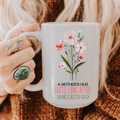 Person holding a 15oz mug with floral design and text 'A Mother's Hug Lasts Long After She Lets Go'