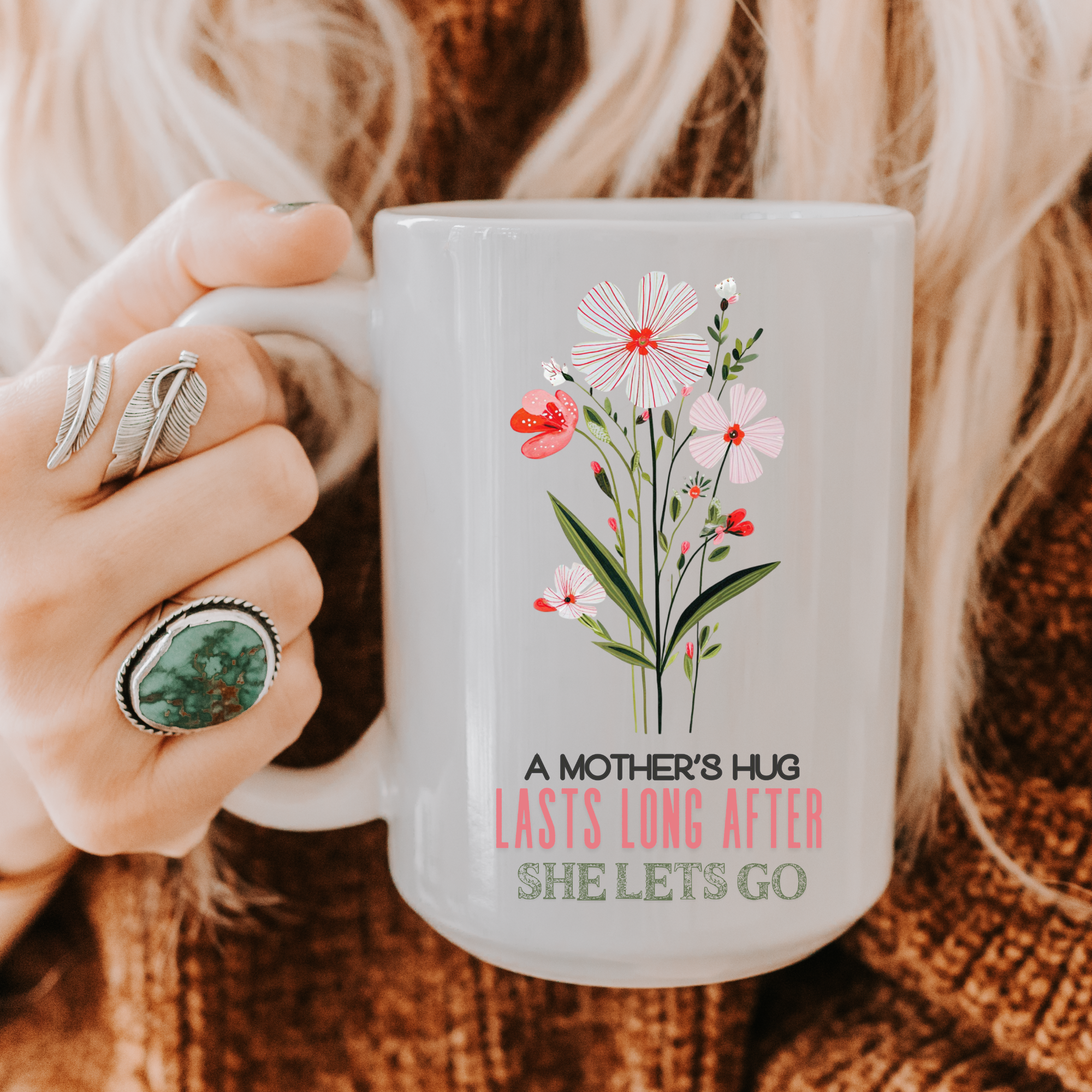 Person holding a 15oz mug with floral design and text 'A Mother's Hug Lasts Long After She Lets Go'