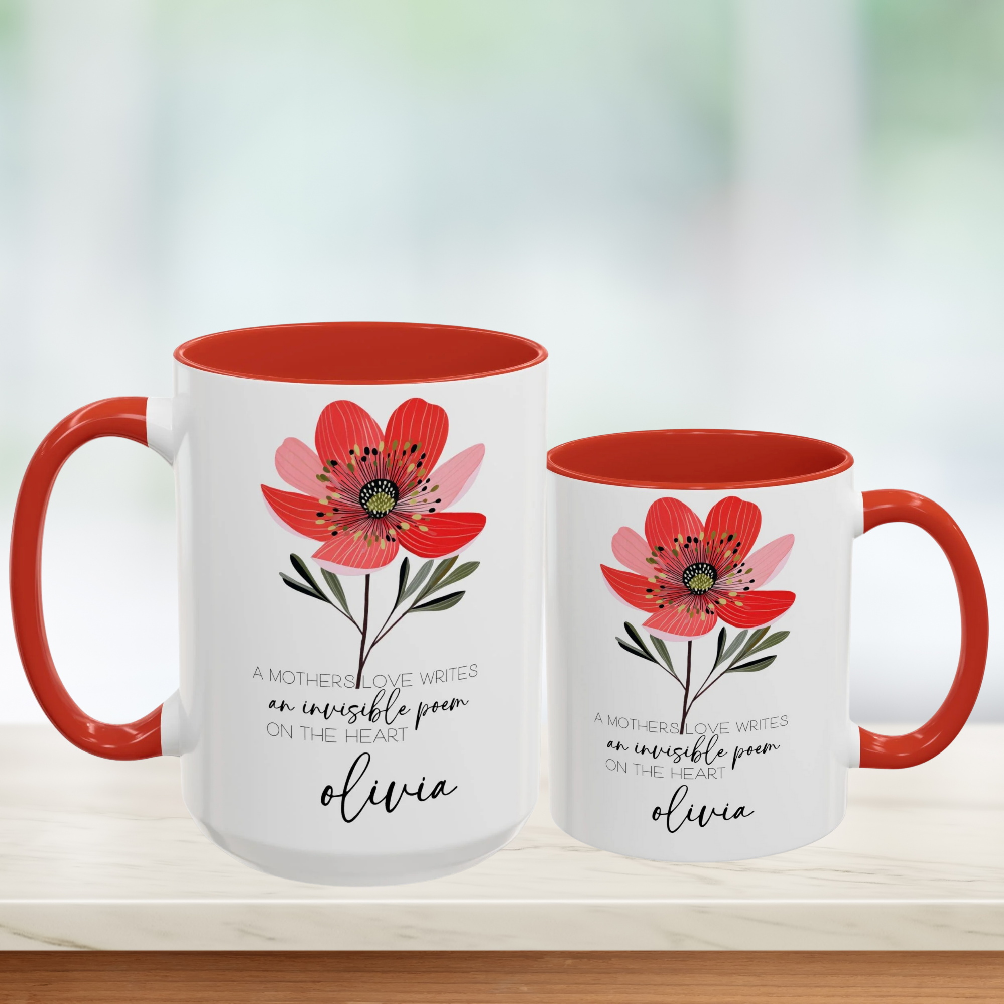 Two white mugs with red interior and handle, featuring a floral design and text on a blurred background.