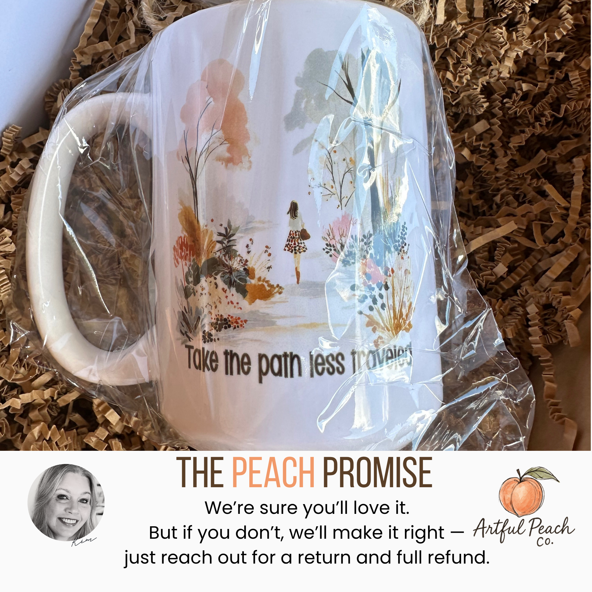 Mug with artistic design and text 'Take the path less traveled' wrapped in plastic on a textured surface.