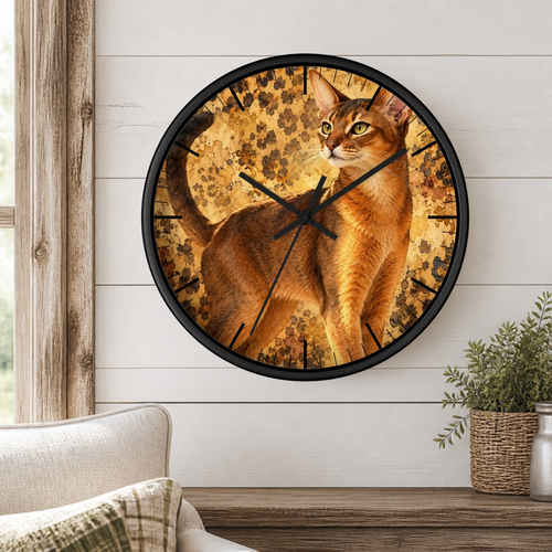Round wall clock with a black frame and a printed cat face design, mounted on a white shiplap wall above a wooden shelf with a plant and part of a sofa visible.