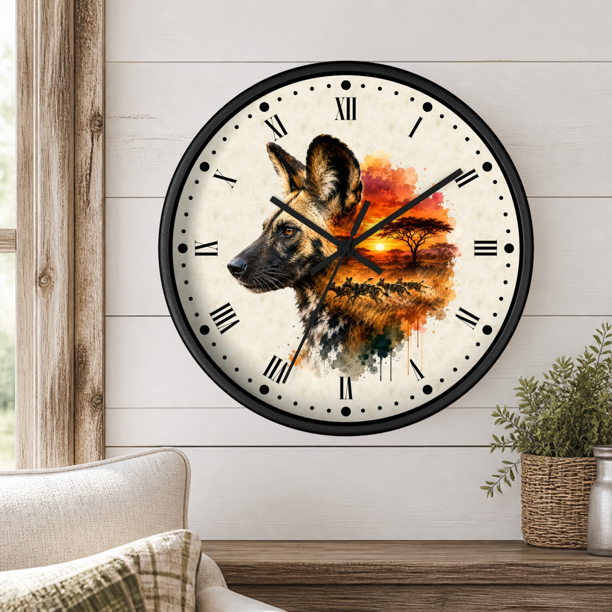 A round wall clock with a black frame and a watercolor-style African wild dog portrait on the face, mounted on a white shiplap wall above a wooden table with a plant and part of a sofa visible.