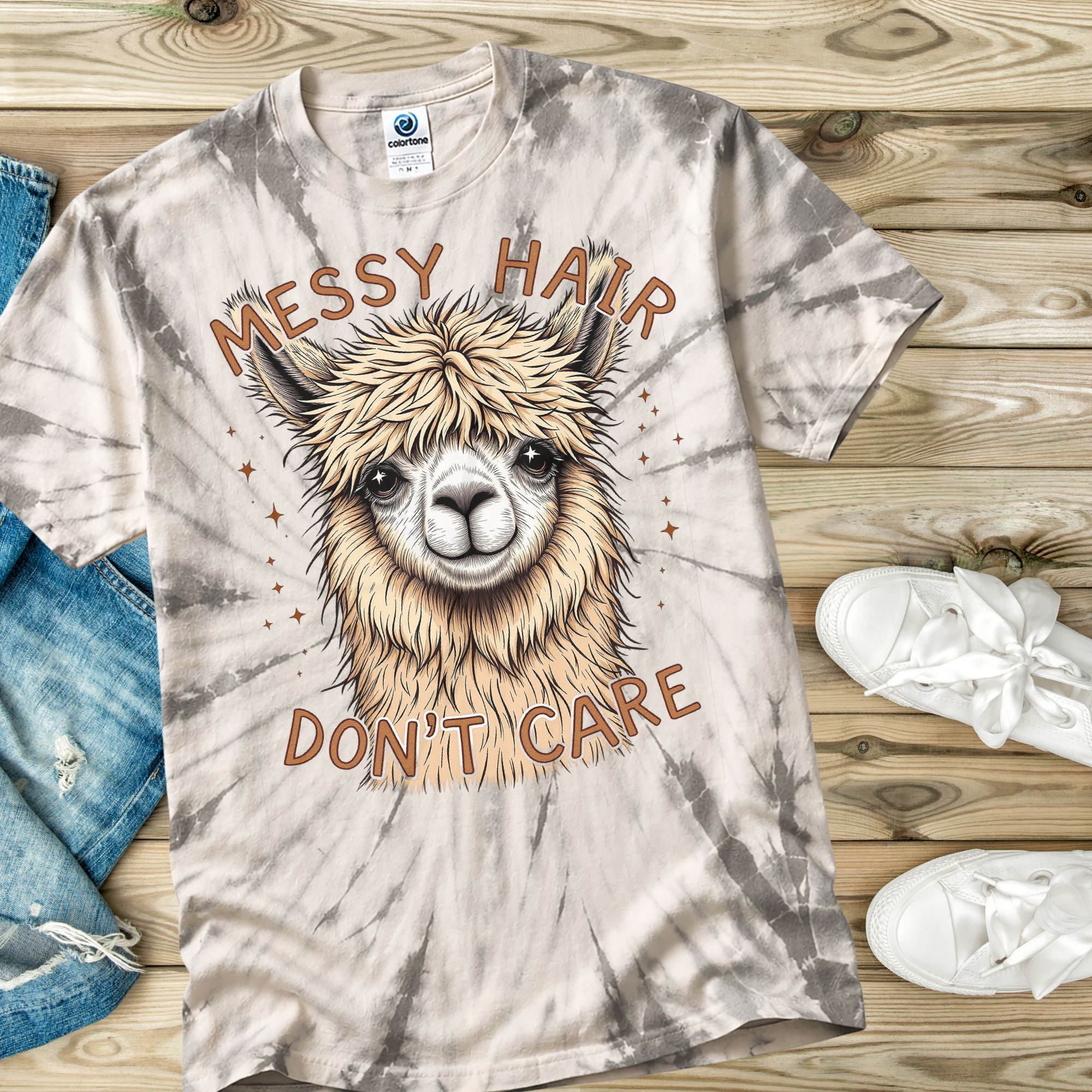 Tie-dye t-shirt with a llama graphic and 'Messy Hair Don't Care' text on a wooden surface.