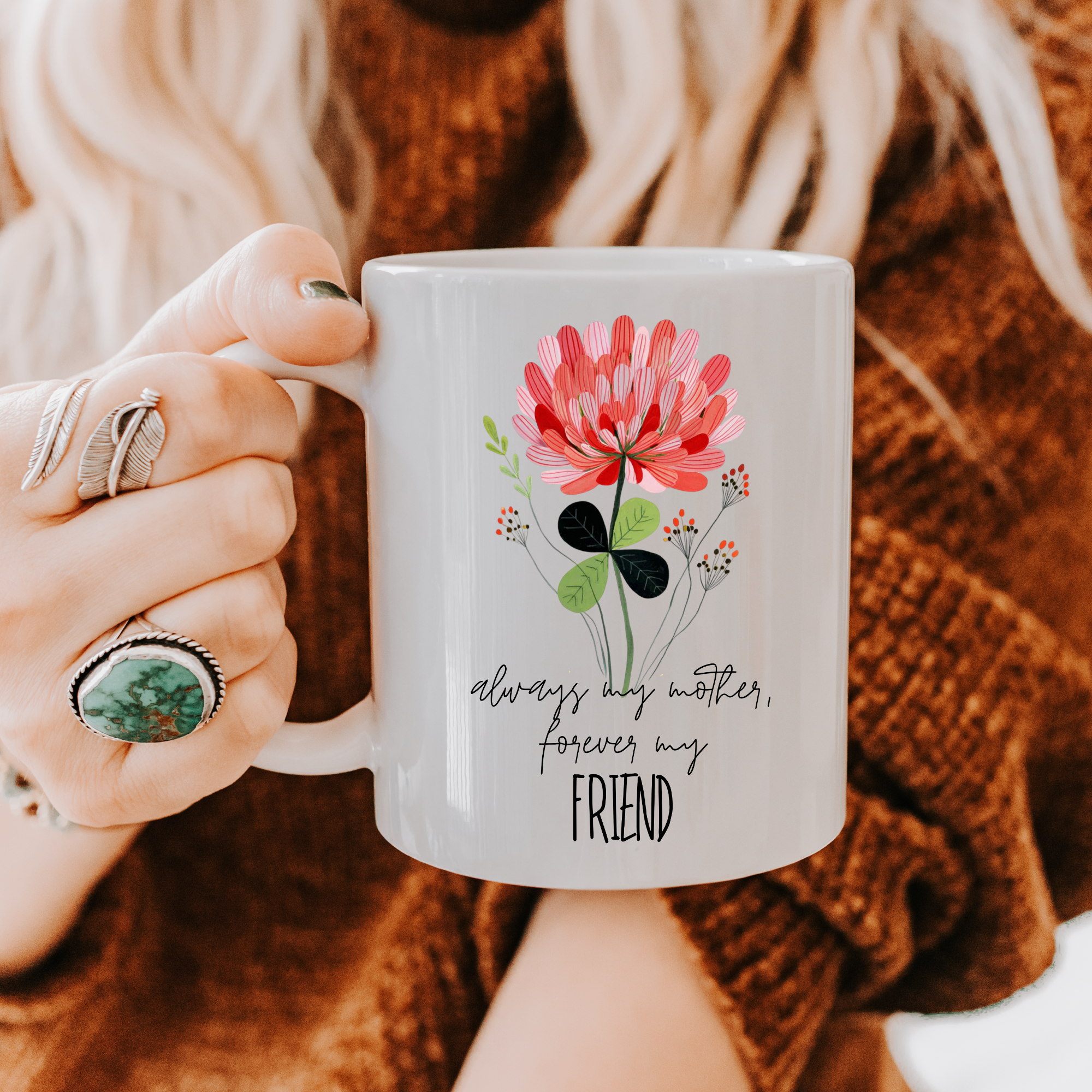 Person holding an 11oz mug with floral design and text 'Always my mother forever my friend', wearing a brown sweater.
