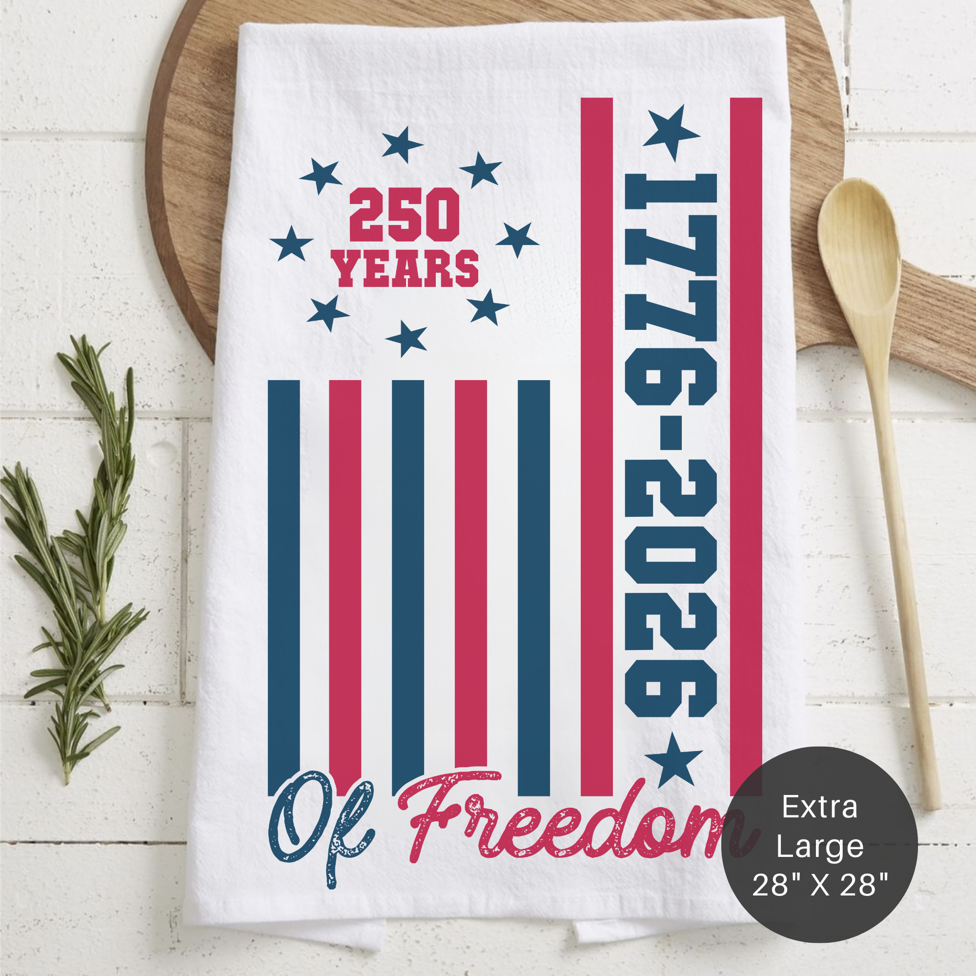 Tea towel with 1776-2026 design on a wooden board with utensils.