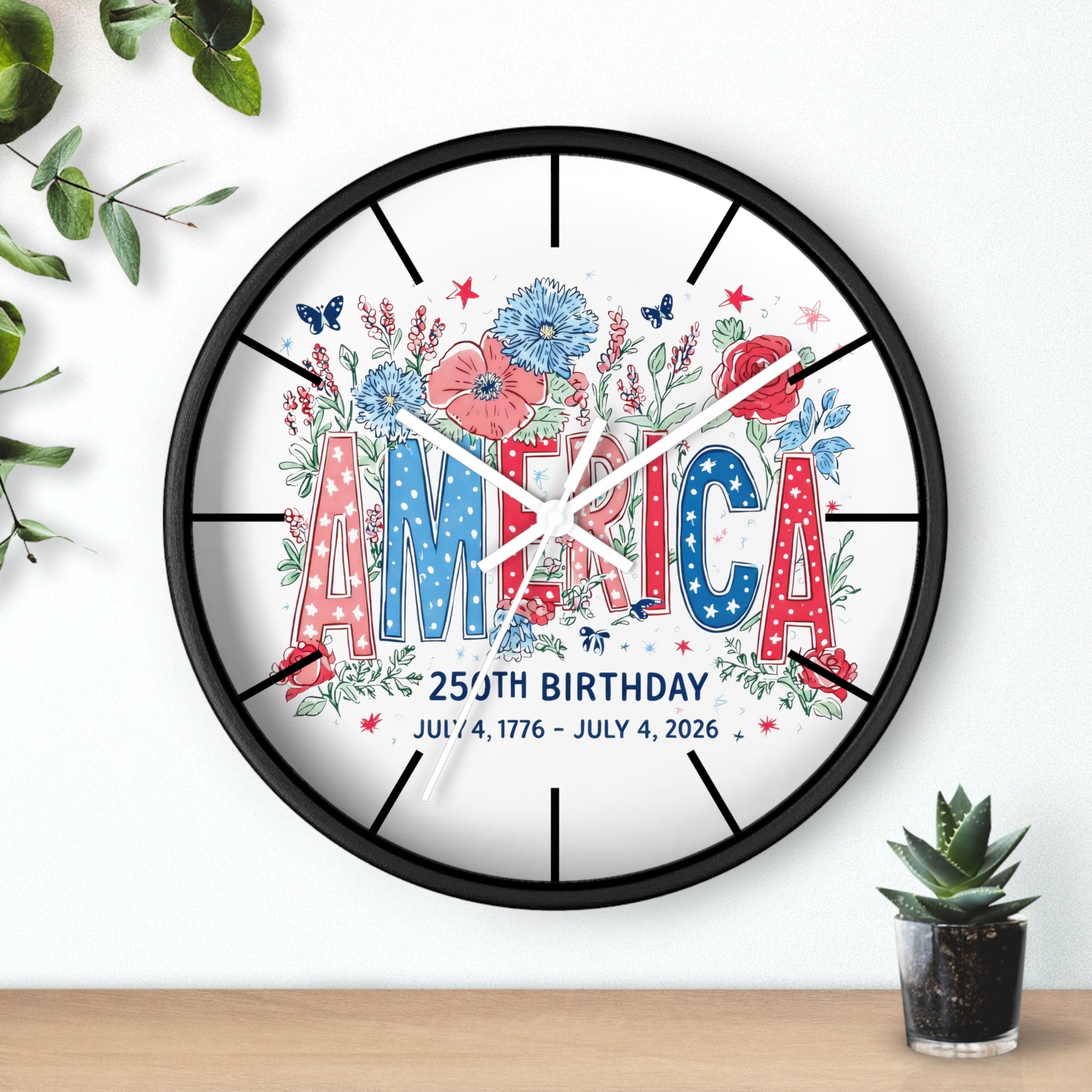 Round black decorative wall clock with white hands and 'AMERICA' and floral design on a white background