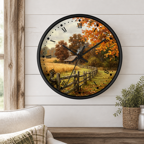 Round wall clock with a black frame and a scenic autumn landscape print featuring orange and yellow foliage, a rustic cabin, and a wooden fence, mounted on a white shiplap wall above a wooden shelf with a plant.