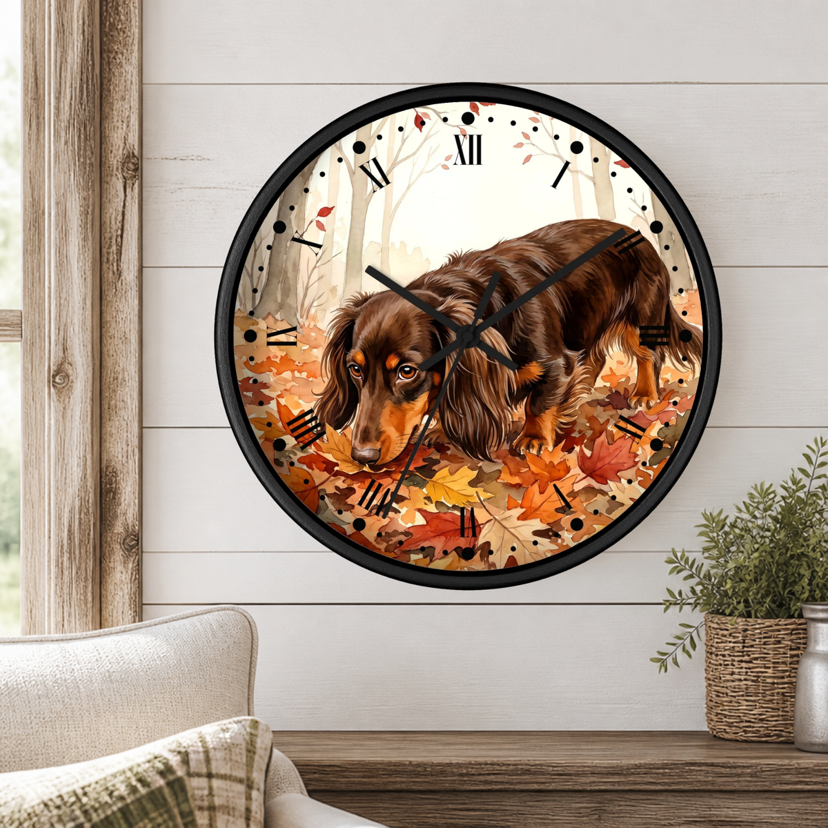 A round wall clock with a black frame and Roman numerals, featuring an illustration of a brown dachshund walking through orange autumn leaves. The clock is mounted on a white shiplap wall above a wooden mantel with a small potted plant.