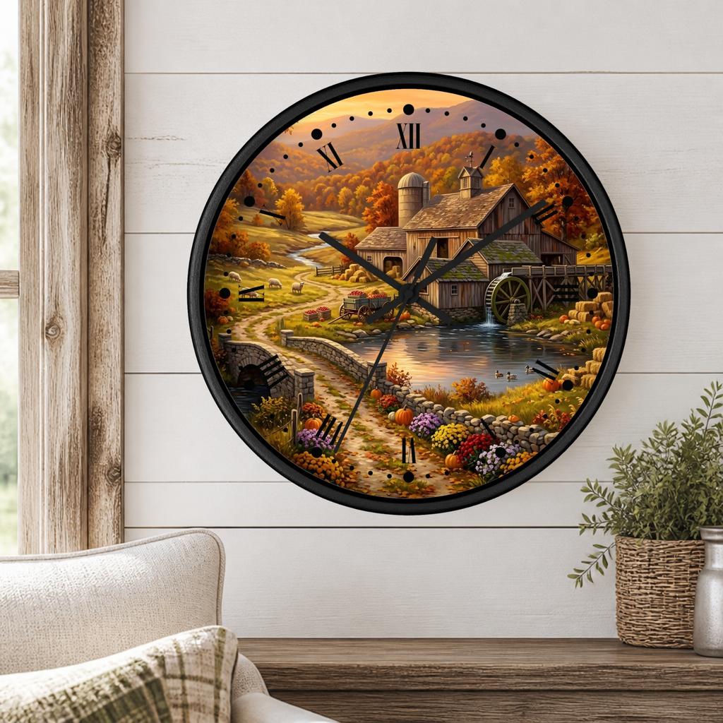 A round wall clock with a black frame and a scenic autumn farm illustration, mounted on a white shiplap wall above a wooden table with a potted plant.
