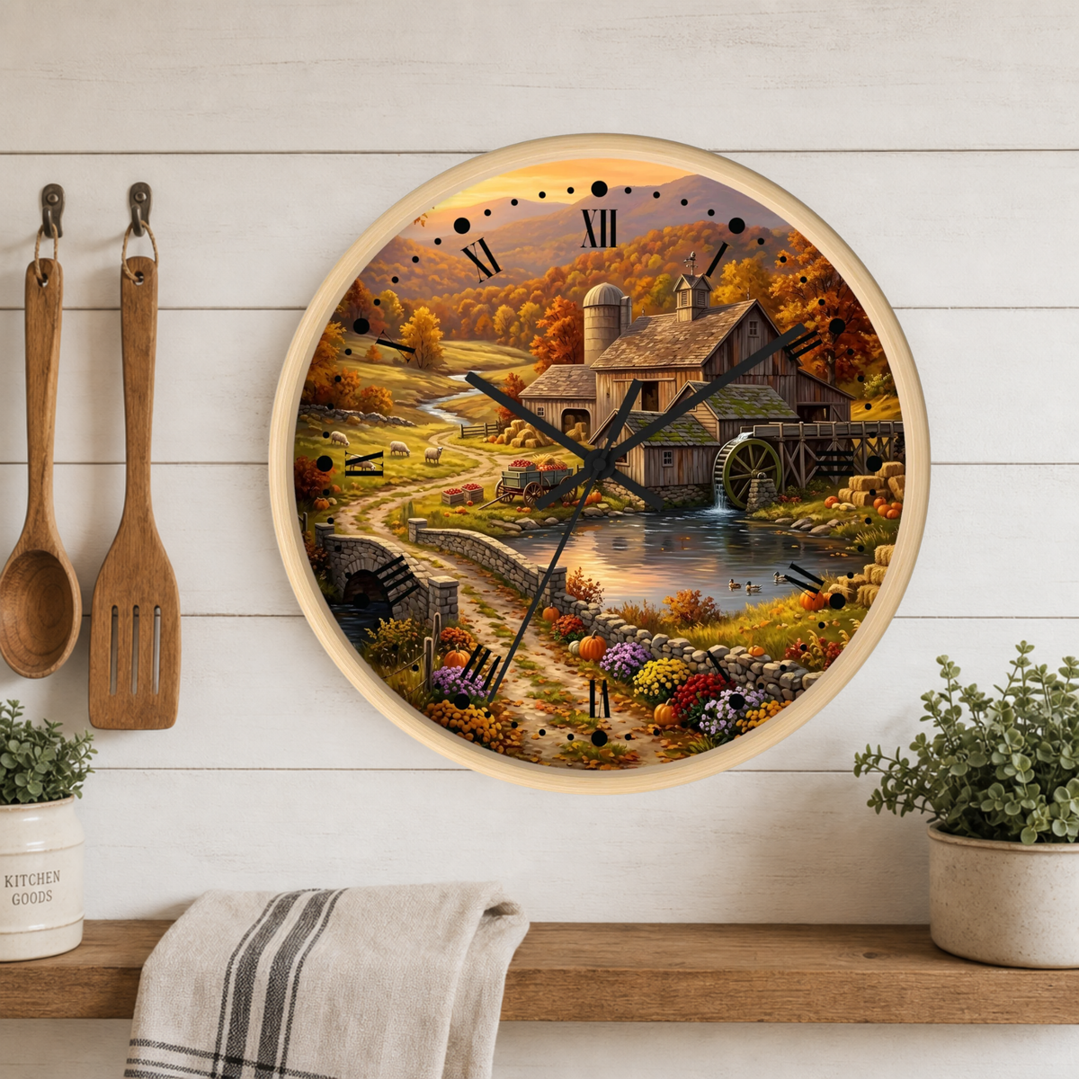 Round wall clock with a rustic country watermill landscape print, mounted on a white wood plank wall above a wooden shelf with kitchen utensils and potted plants.
