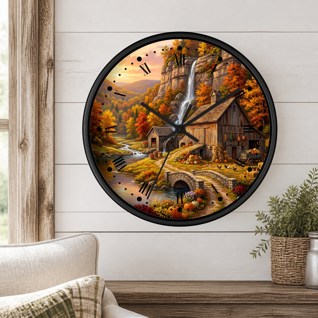 A round wall clock with a black frame and a detailed autumn landscape print featuring a waterfall, cabin, bridge, and colorful fall foliage, mounted on a white shiplap wall above a wooden table with a plant and part of a chair visible.