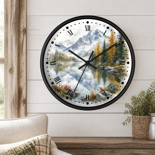 A round wall clock with a scenic mountain lake print, mounted on a white wood-paneled wall above a wooden table with a potted plant and part of a sofa visible.