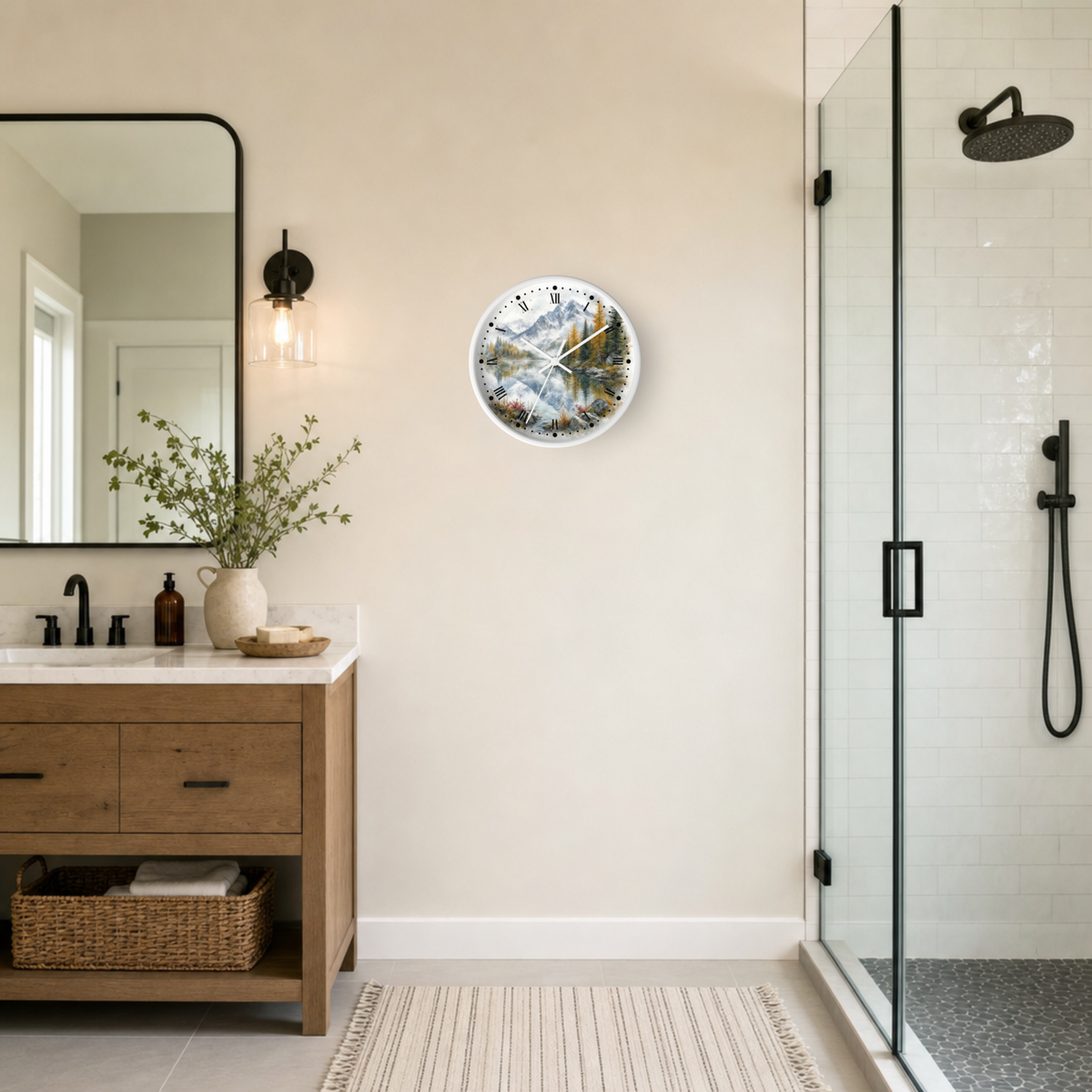 A round wall clock with a scenic mountain landscape print hangs on a beige wall in a modern bathroom setting next to a wooden vanity and a glass shower enclosure.
