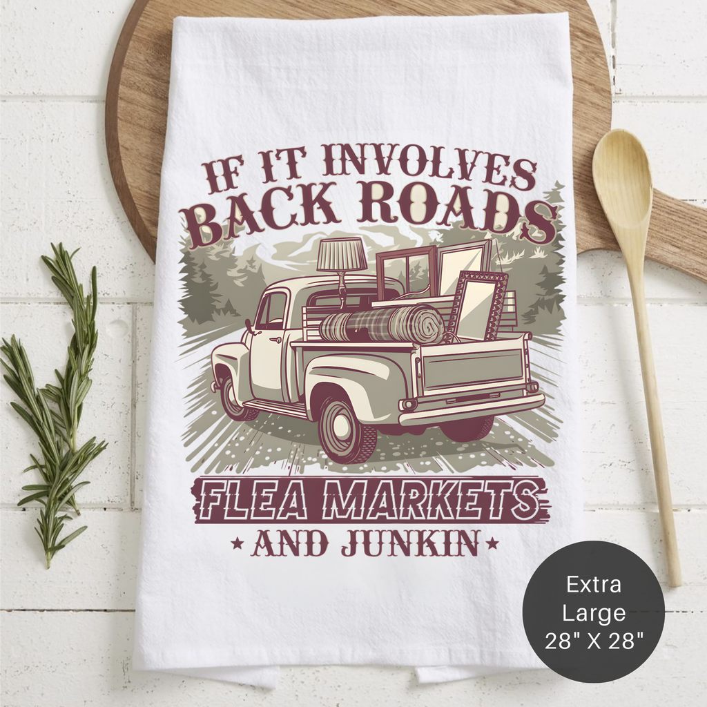 Tea towel with a vintage truck graphic and text 'If It Involves Back Roads Flea Markets and Junkin' on a wooden surface.