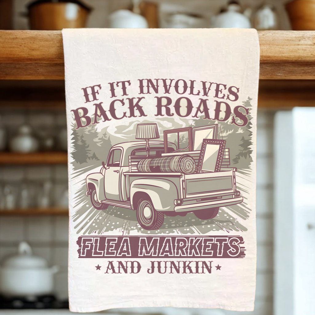 Kitchen towel with a truck graphic and text about back roads, flea markets, and junkin' hanging on a wooden rack.