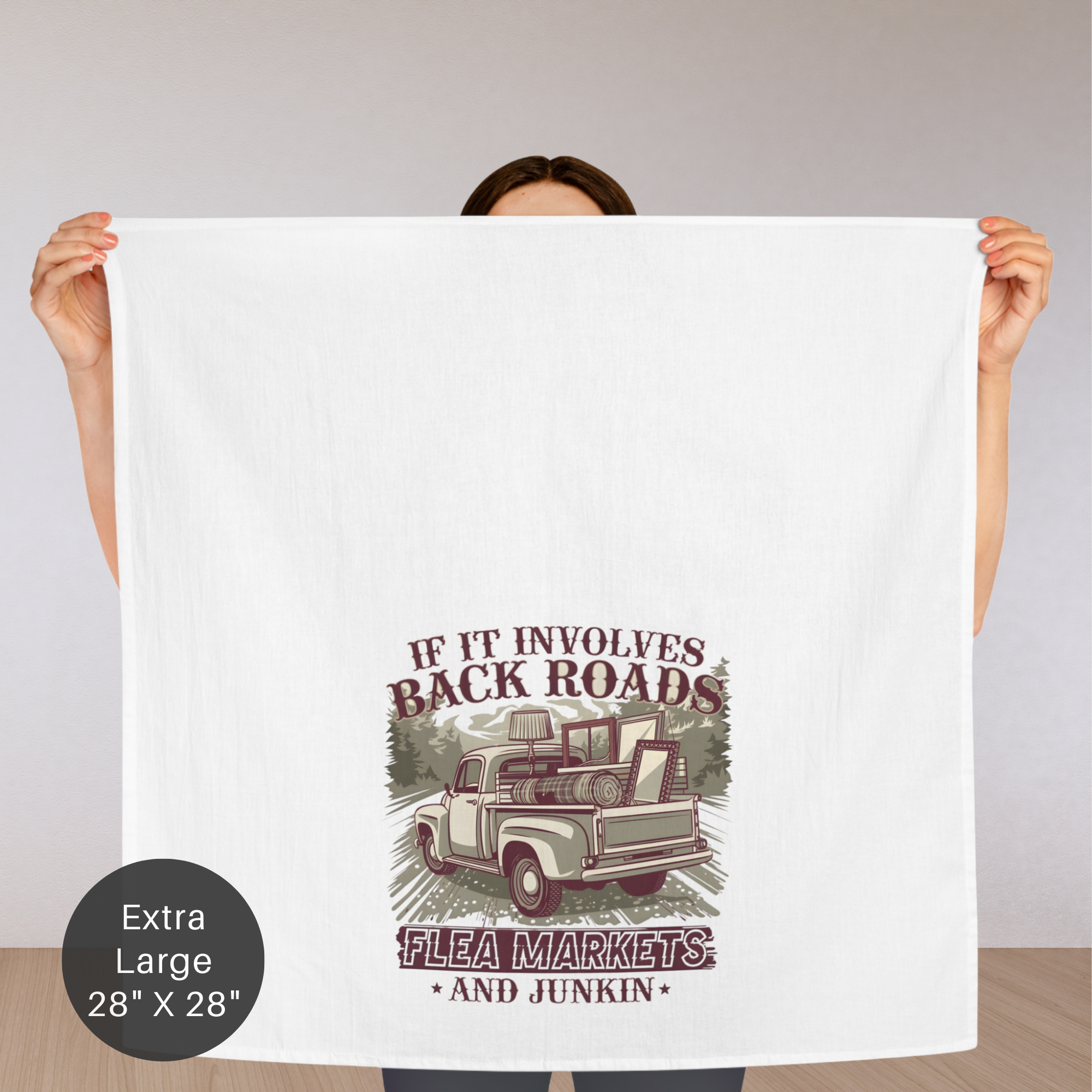 Person holding a towel with a graphic design of a truck, text ' If It Involves Back Roads Flea Markets and Junkin' on a white background.