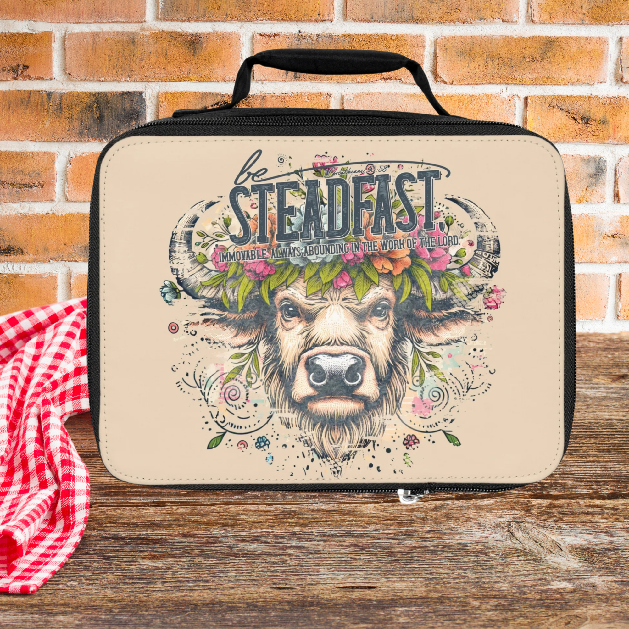 Beige lunch bag with bull graphic and 'be Steadfast' text on a brick wall background