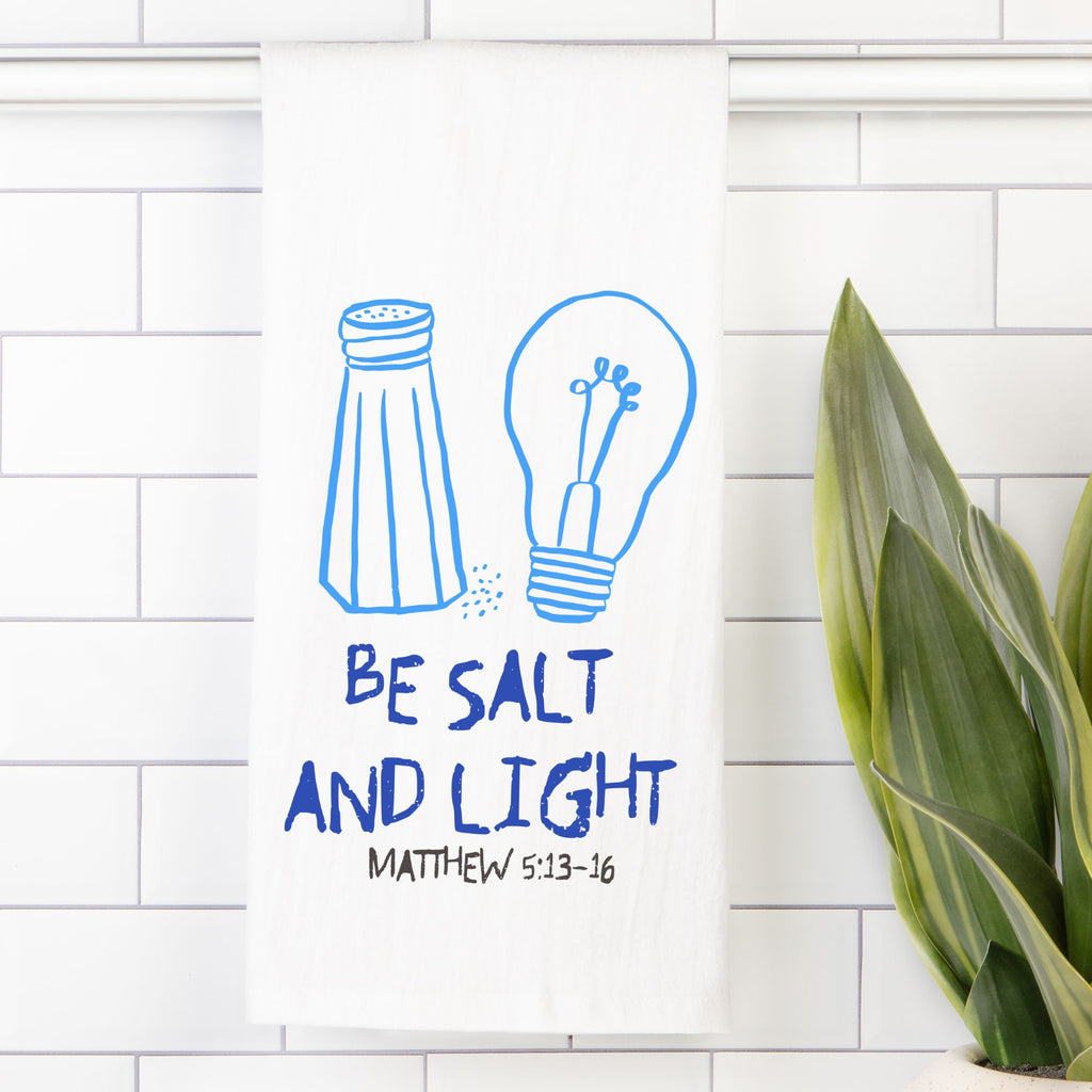 Tea towel with an Illustration of a salt shaker and light bulb with 'Be Salt and Light' text on a white tiled background.