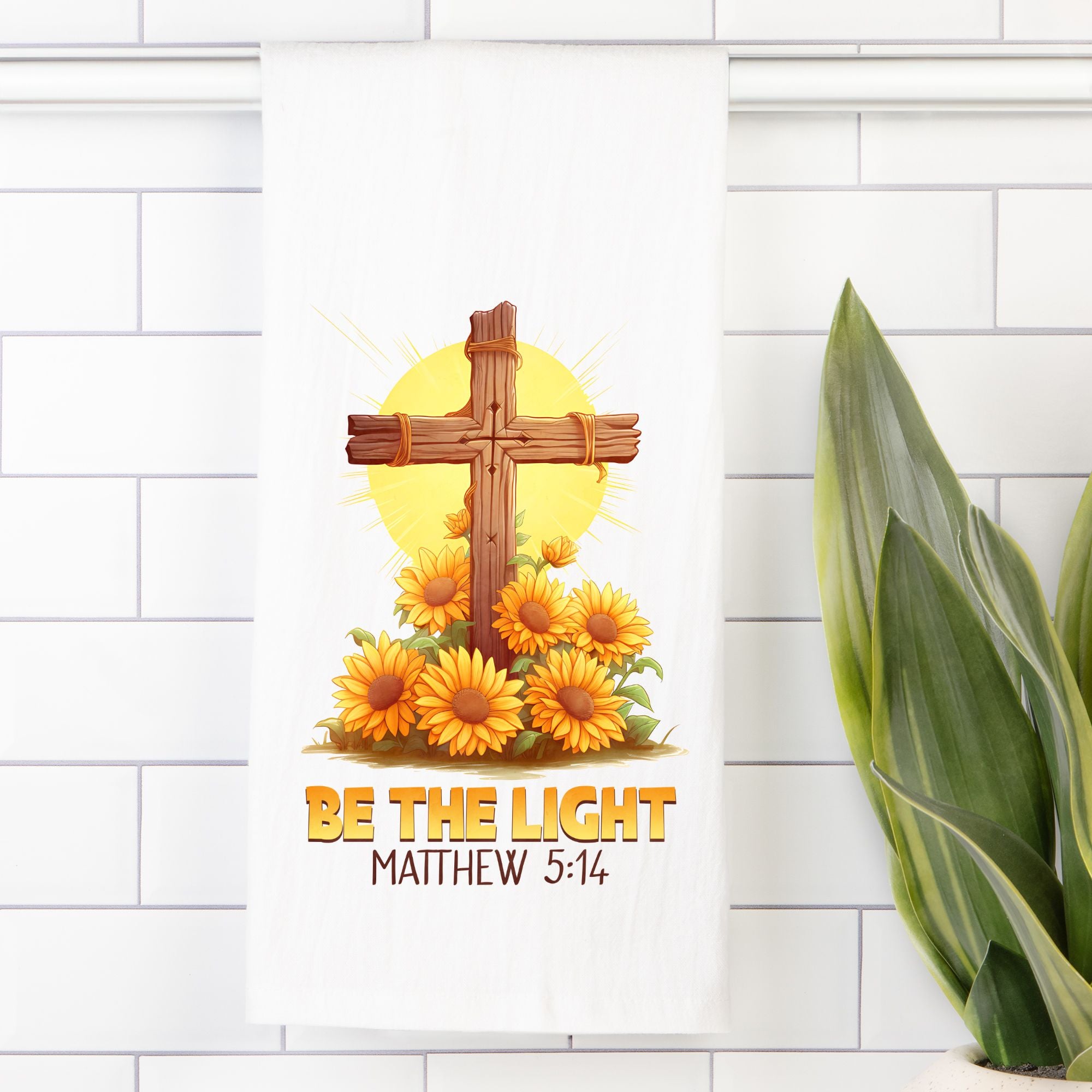 Decorative tea towel with cross, sun, and flowers on a white tiled wall.