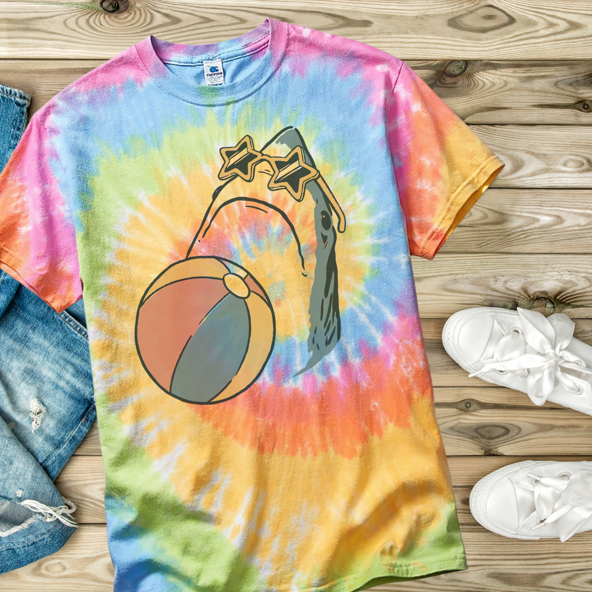 Tie-dye t-shirt in the color Eternity with a hand drawn shark with a beach ball and wearing star shaped sunglasses design on a wooden surface.