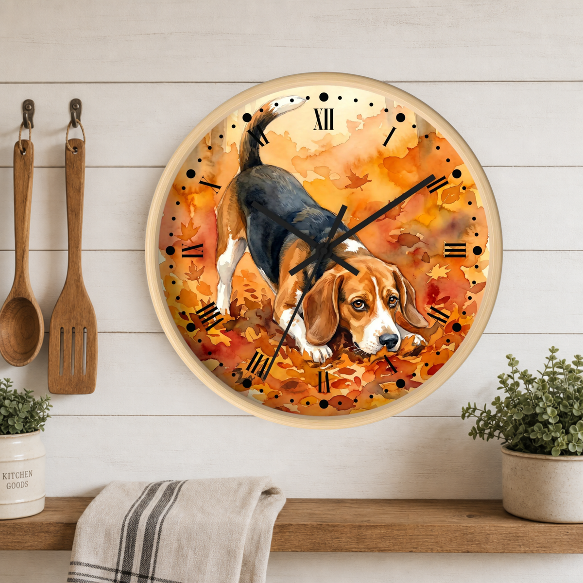 A round wall clock with a watercolor-style beagle illustration over autumn leaves, mounted on a white wood plank wall above a shelf with plants and kitchen utensils.
