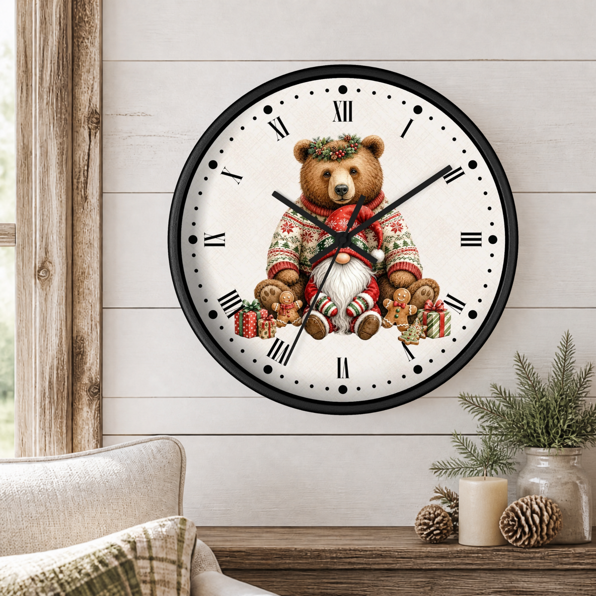 A round wall clock with a black frame and a white face featuring an illustrated teddy bear in a red knit sweater and Santa hat, styled on a light wood paneled wall above a table with pine branches and candles.