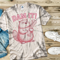 Tie-dye t-shirt with a beaver graphic and 'DAM IT!' text on a wooden surface.