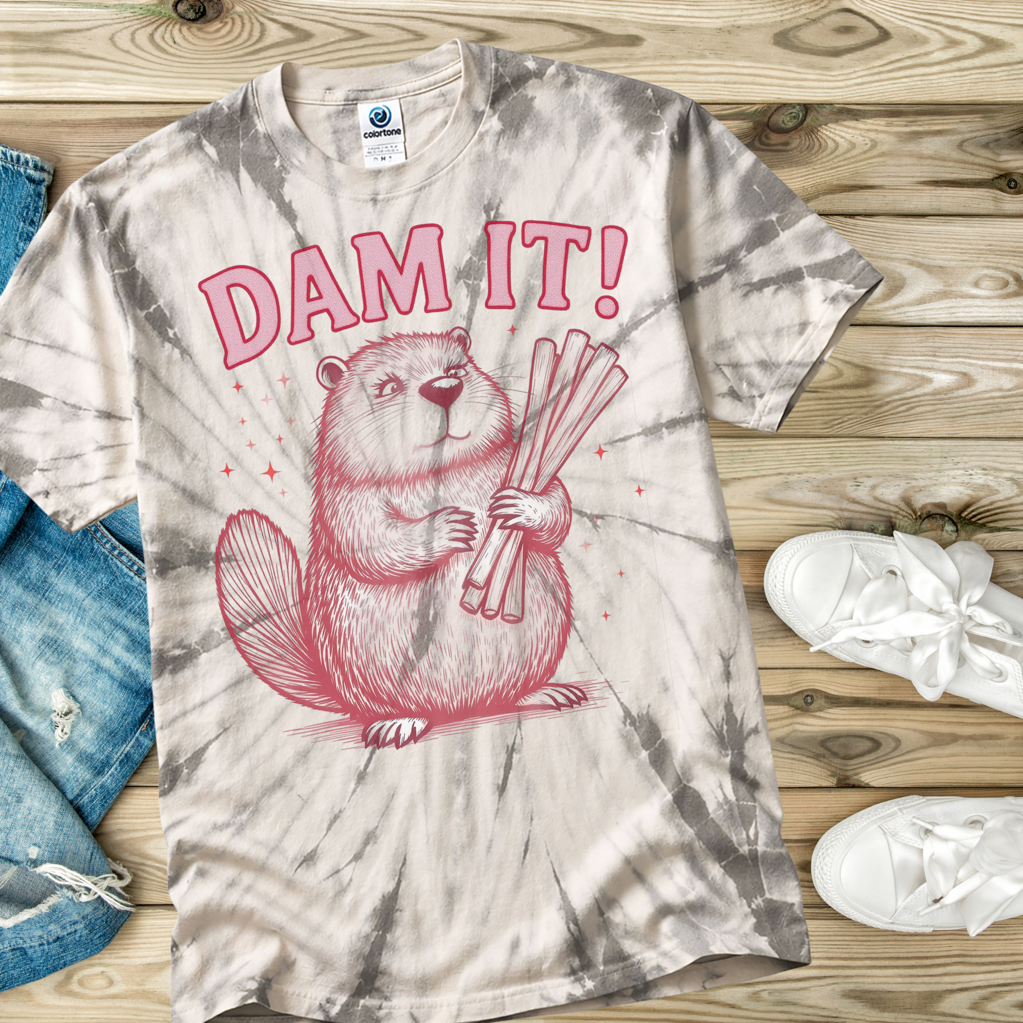 Tie-dye t-shirt with a beaver graphic and 'DAM IT!' text on a wooden surface.