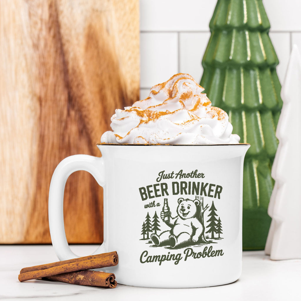 White mug with bear graphic and text, filled with hot chocolate and whipped cream, on a wooden surface.