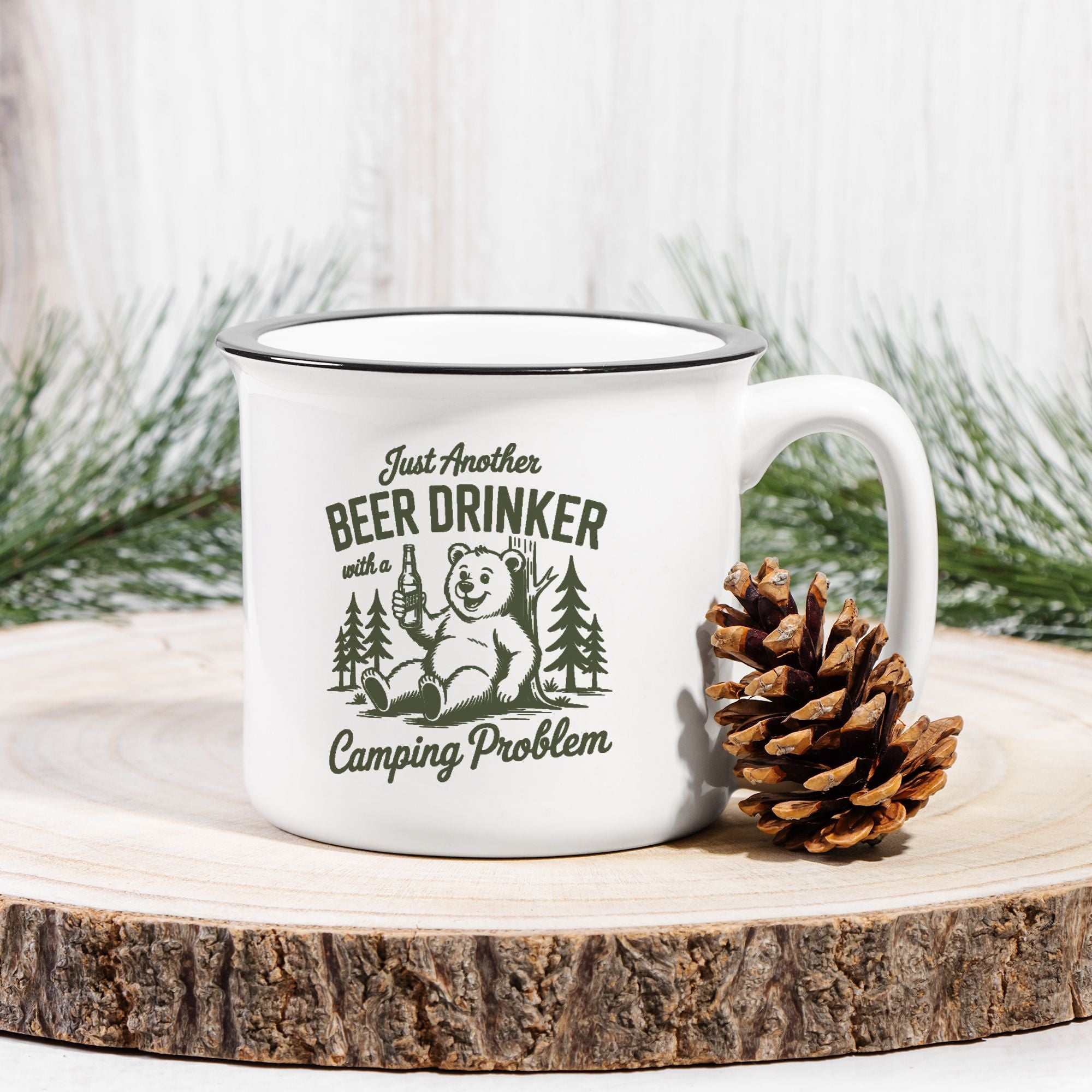 White mug with bear graphic and text on a wooden surface with a pine cone and evergreen branches.
