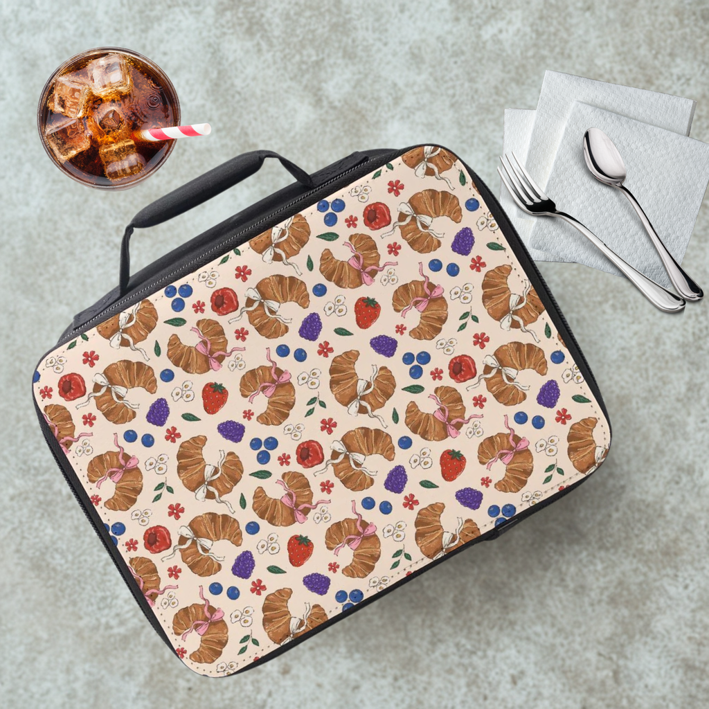 Lunch bag with croissant pattern on a cafeteria table with a drink and utensils.